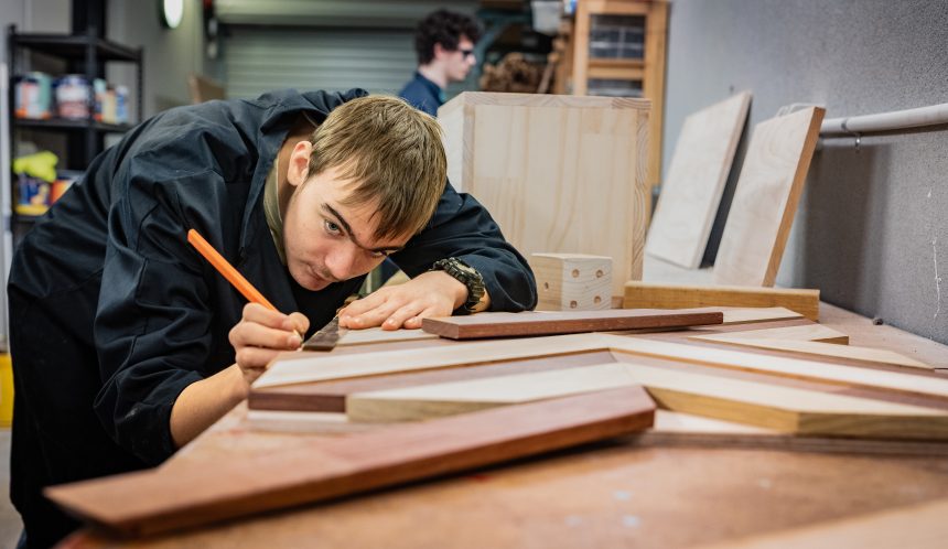 Student measuring wood cutouts with a metal ruler and pencil