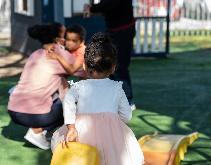 A child hugging their mother while another plays